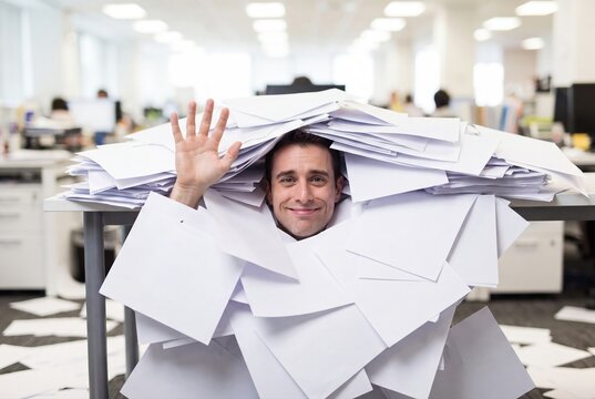 Overwhelmed businessman buried under stack of paperwork in office