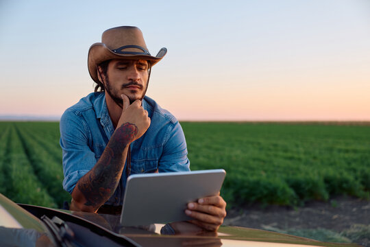 Farm worker using digital tablet while leaning on his truck in field.