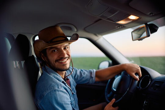 Young happy farmer driving his truck and looking at camera.