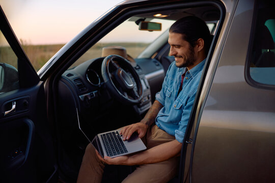 Happy farmer using laptop while sitting inside of his pickup truck.