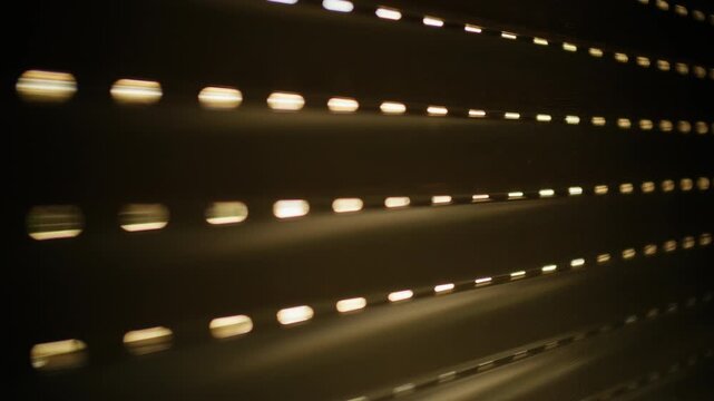 Window roller shutter partially closed, creating horizontal lines of light and shadow, forming an abstract pattern