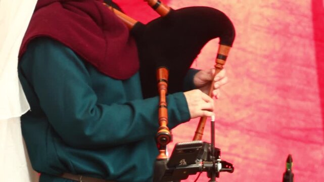 A person in medieval attire plays the bagpipes on a scenic background