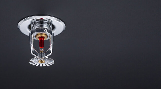 Fire sprinkler mounted on the ceiling for emergency facility protection. Automatic water suppression system as a safety measure against building blaze. Firefighting equipment and gear.