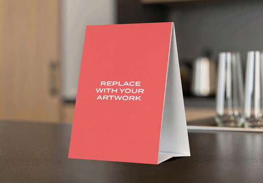 Vertical table tent sign mockup on a dark countertop in modern kitchen setting with glassware and appliances the background, interior display blurred Template