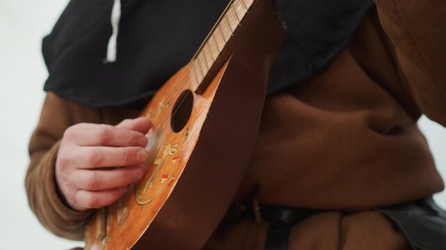 Tight chest-level close-up of person playing small wooden mandolin-like instrument, right hand actively strumming and plucking strings while left arm supports body, with visible finger movement and