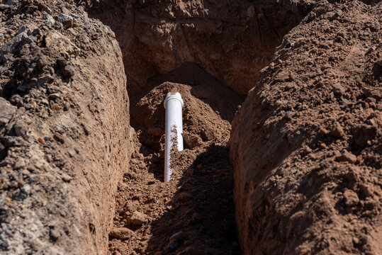 White PVC pipe installed inside an earthen trench during underground utility work