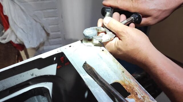 Man repairing washing machine water inlet pipe at home, close-up of hands using wrench on rusty metal connection.