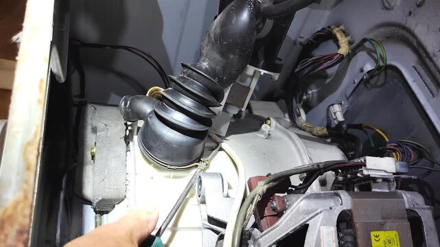 Man repairing washing machine internal motor and pump components at home, close-up of hand inspecting black mechanism with wiring.