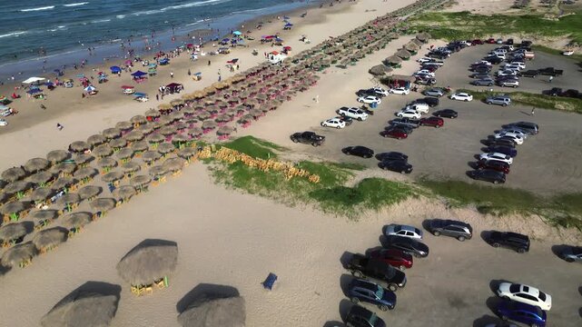 Miramar Beach parking area crowded with vehicles, beachgoers and palapas along the busy Gulf of Mexico shoreline