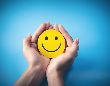 World Mental Health Day concept: a happy smiley face held in caring hands against a blue background.