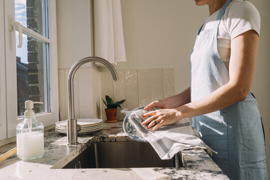 Bright kitchen scene with a person wiping dishes while standing at the sink