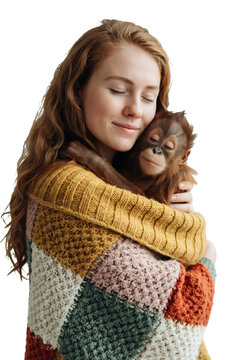 Gentle moment between a woman with long red hair and a baby orangutan resting peacefully inside a multicolor knitted