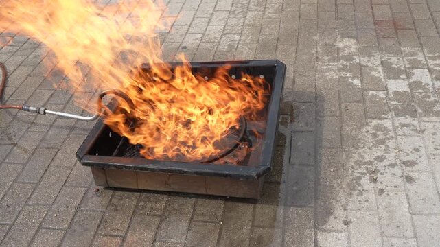 Water extinguishing roaring flames inside a metal training pan during a professional fire safety and emergency response training session