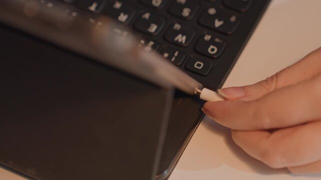 Close up of hand connecting various cables. White audio jack is inserted into available port on device followed. Scene focuses on hands interacting with tablets laptops chargers