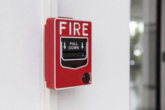 A red fire alarm pull station is mounted on a white wall indoors.