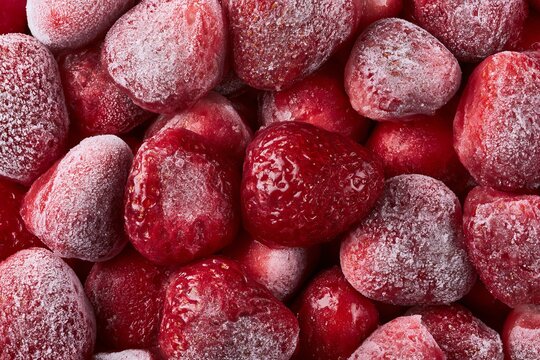 Frozen strawberries are piled together on a surface showing their bright red color and icy texture