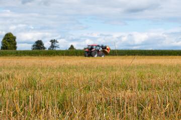 Red tractor working in a harvested agricultural field, farm machinery for farming and crop production under dramatic cloudy sky © Iryna
