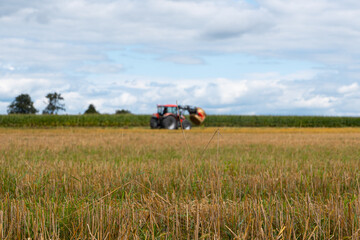 Red tractor working in a harvested agricultural field, farm machinery for farming and crop production under dramatic cloudy sky © Iryna