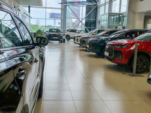 Modern car dealership interior. Polished vehicles line the showroom floor. Large windows flood the space with light. People examine cars with interest. Perfect for automotive marketing. Moscow