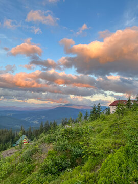 Scenic mountain landscape with colorful sunset clouds over rolling hills and a house on a grassy slope