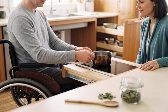Wheelchair user cooking at a lowered accessible kitchen cooktop with a therapist