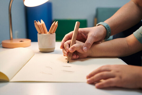Therapist guiding a child hand on a thick pencil during handwriting practice
