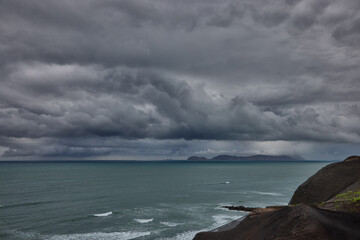 storm clouds roll over San Lorenzo Island as seen from the cliffs of Miraflores, Lima, casting a moody, atmospheric veil over the Pacific coastline. The dense cloud formations and shifting light hint  © Beto Santillan