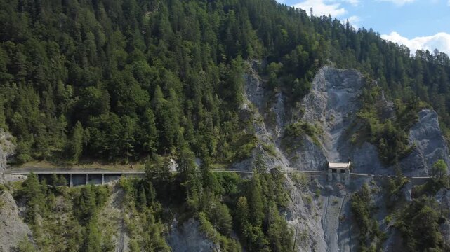 Waldbedeckte Felswand mit Stra&szlig;e und Galerie &ndash; gr&uuml;ne Alpenlandschaft aus der Vogelperspektive