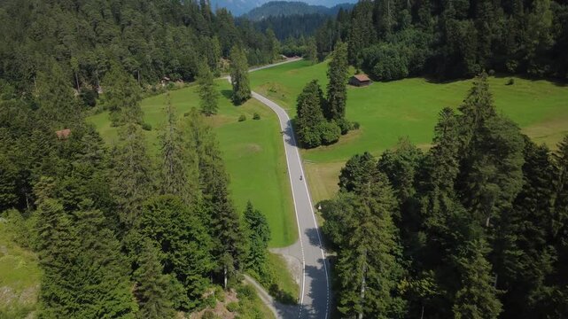 Geschwungene Passstra&szlig;e mit S-Kurven durch gr&uuml;ne Alm mit Nadelb&auml;umen &ndash; Luftaufnahme einer Alpen-Velotour