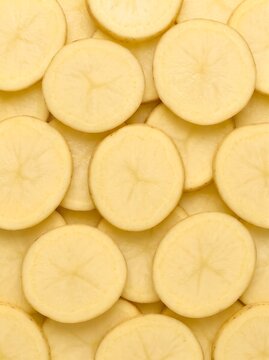 Raw yellow potato slices create a repeating organic pattern and smooth vegetable texture in this potrait orientation for food blog graphics, cookbook layouts, and culinary website backgrounds.