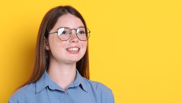 Beautiful girl with freckles wearing glasses on orange background, space for text