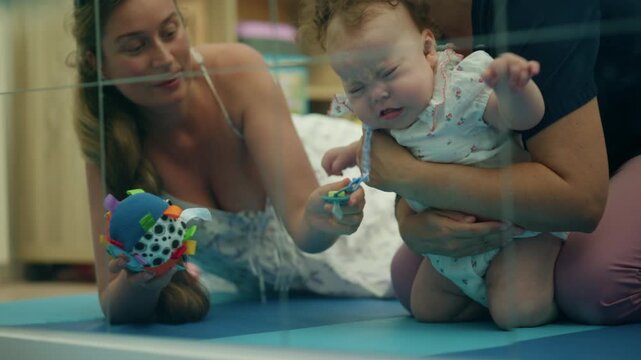 Baby learning to crawl during a physical therapy session, supported by a professional therapist, with mother observing