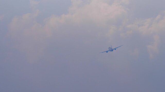 Passenger airplane flying through soft clouds in hazy blue sky. Commercial airliner banking during flight. Long telephoto shot of jet plane in mid air.