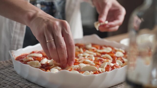 Woman adds pieces of mozzarella to gnocchi covered with tomato sauce in a baking dish. Concept of homemade Italian cooking and preparing dinner for the oven