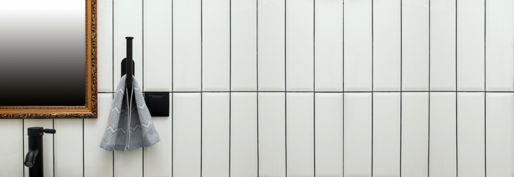 Modern bathroom interior featuring white vertical subway tiles with copy space next to a mirror, black tap, hanging towel. white subway tile bond pattern contrast with black hydrophobic epoxy grout