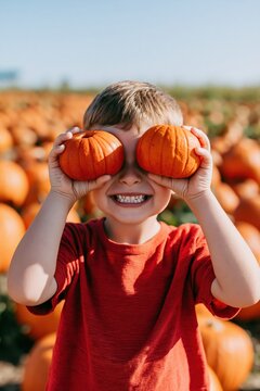 Laughing boy covering eyes with small orange pumpkins in a pumpkin patch for fall harvest background and seasonal banner design