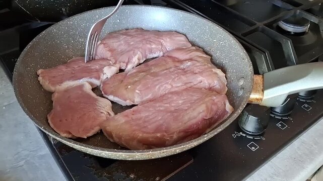 Cooking meat in a pan on the stove with a fork to check doneness while preparing a sauce on another burner