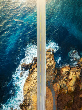 Aerial view of road, sea with waves and stones at sunset in Lofoten Islands, Norway. Landscape with beautiful bridge, transparent blue water, rocks. Top view from drone of highway in summer. Travel