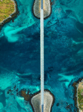 Fredvang bridges road over turquoise ocean water in Lofoten, Norway. Aerial top down drone view of coastal highway, island coast, clear sea bottom, rocks and scenic landscape in autumn