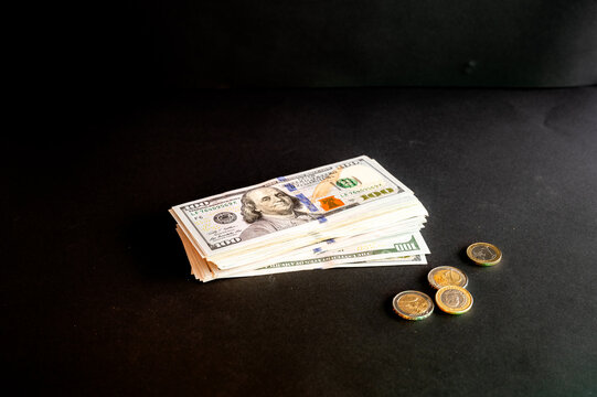 A stack of US hundred dollar bills with euro coins on a dark background a creative concept of money cash savings and income.