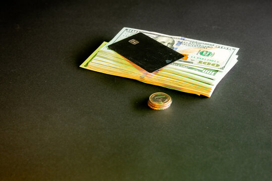 A black bank card on a stack of US dollar bills with a euro coin on a dark background a conceptual image of cashless payment money and finance.