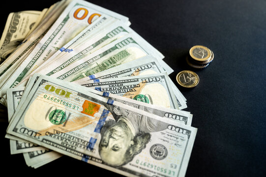 A stack of US hundred dollar bills and euro coins on a dark background a creative concept of money cash and financial success.
