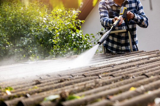 Man cleaning roof from dirt and moss with high pressure washer during home maintenance