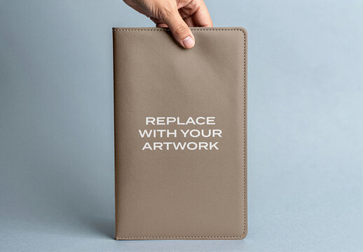 Leather notebook mockup held in hand, vertical orientation with replaceable artwork text, studio background, branding presentation, design template for product display