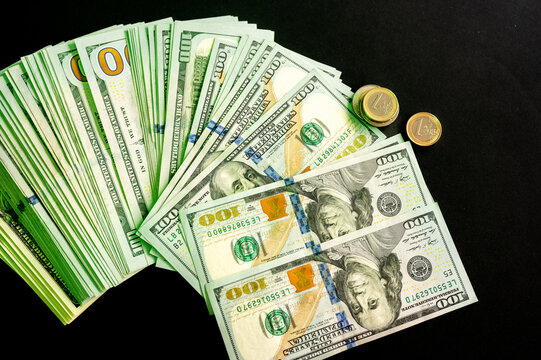 A fan of US hundred dollar bills and coins lit with green light on dark a creative concept of money cash and prosperity.