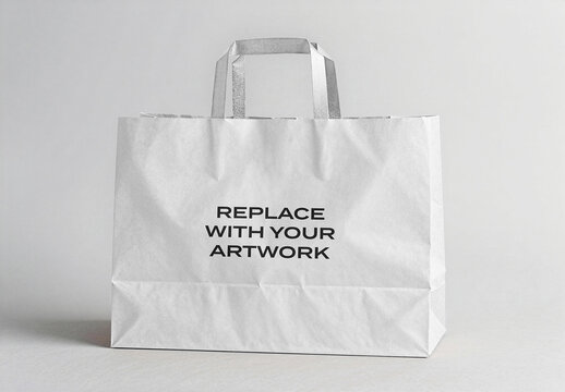 Paper shopping bag mockup with silver handles on a light gray surface, realistic packaging presentation copy space for branding, graphic design template retail and e-commerce