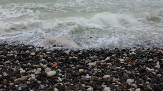 Sea foam washing over wet pebbles at Cap Blanc-Nez, France. Close panning shot of the waterline on a shingle beach with dark flint stones and a chalk boulder on the Opal Coast