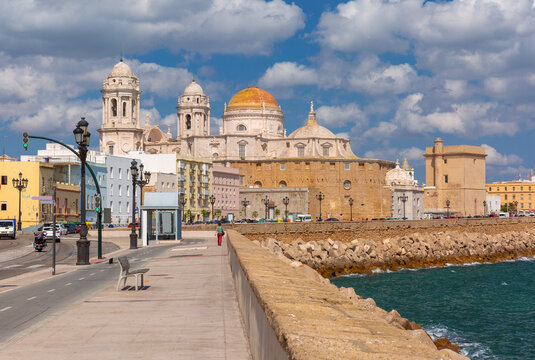 Historic cathedral with its golden dome rises above the coastal promenade and stone seawall in Cadiz, Spain.