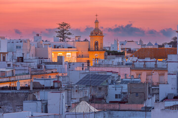 White rooftops and an illuminated bell tower under a colorful sunset sky in the historic center of Cadiz, Andalusia, Spain. © Kavalenkava