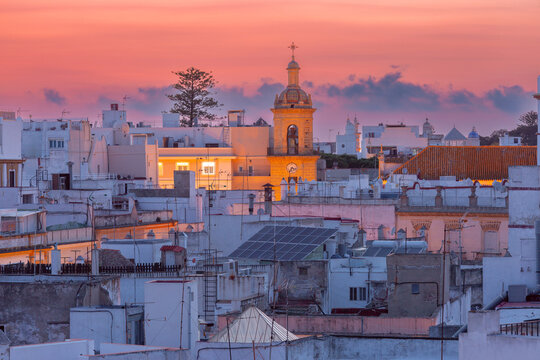 White rooftops and an illuminated bell tower under a colorful sunset sky in the historic center of Cadiz, Andalusia, Spain.